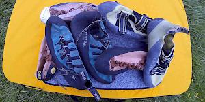 The picture shows a pile of climbing shoes of varying ages spread out on a bouldering pad.