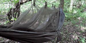 Image of the Snugpak Jungle Hammock pitched in woodland with the integrated mosquito net suspended above and a sleeping bag inside..